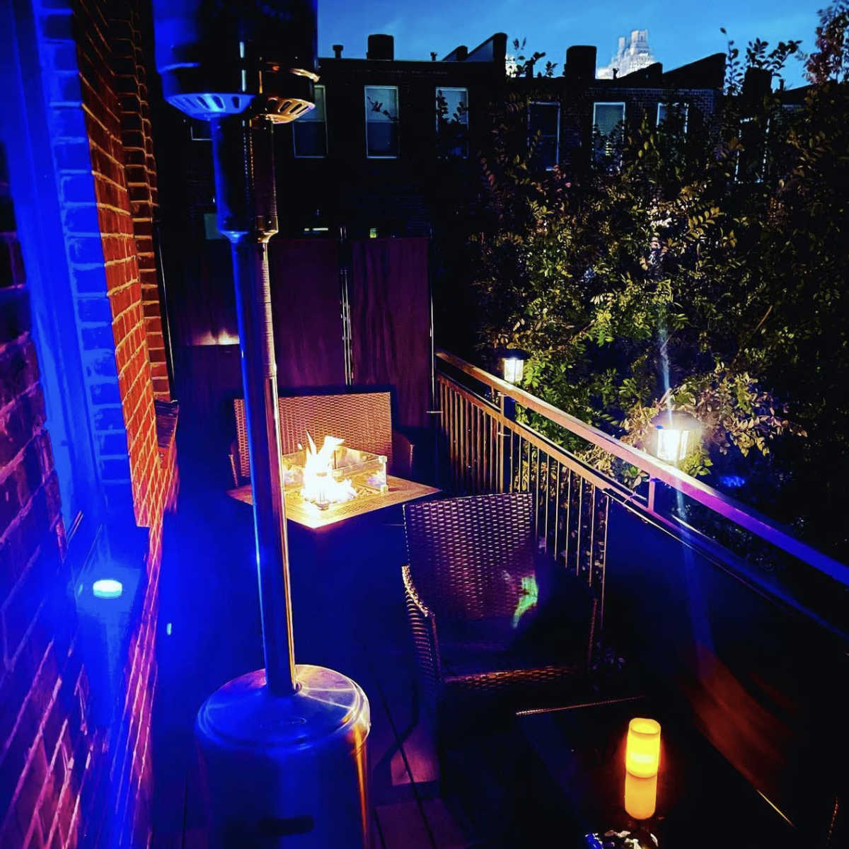 A cozy balcony with a patio heater, wicker furniture, and soft lighting is visible at night.
