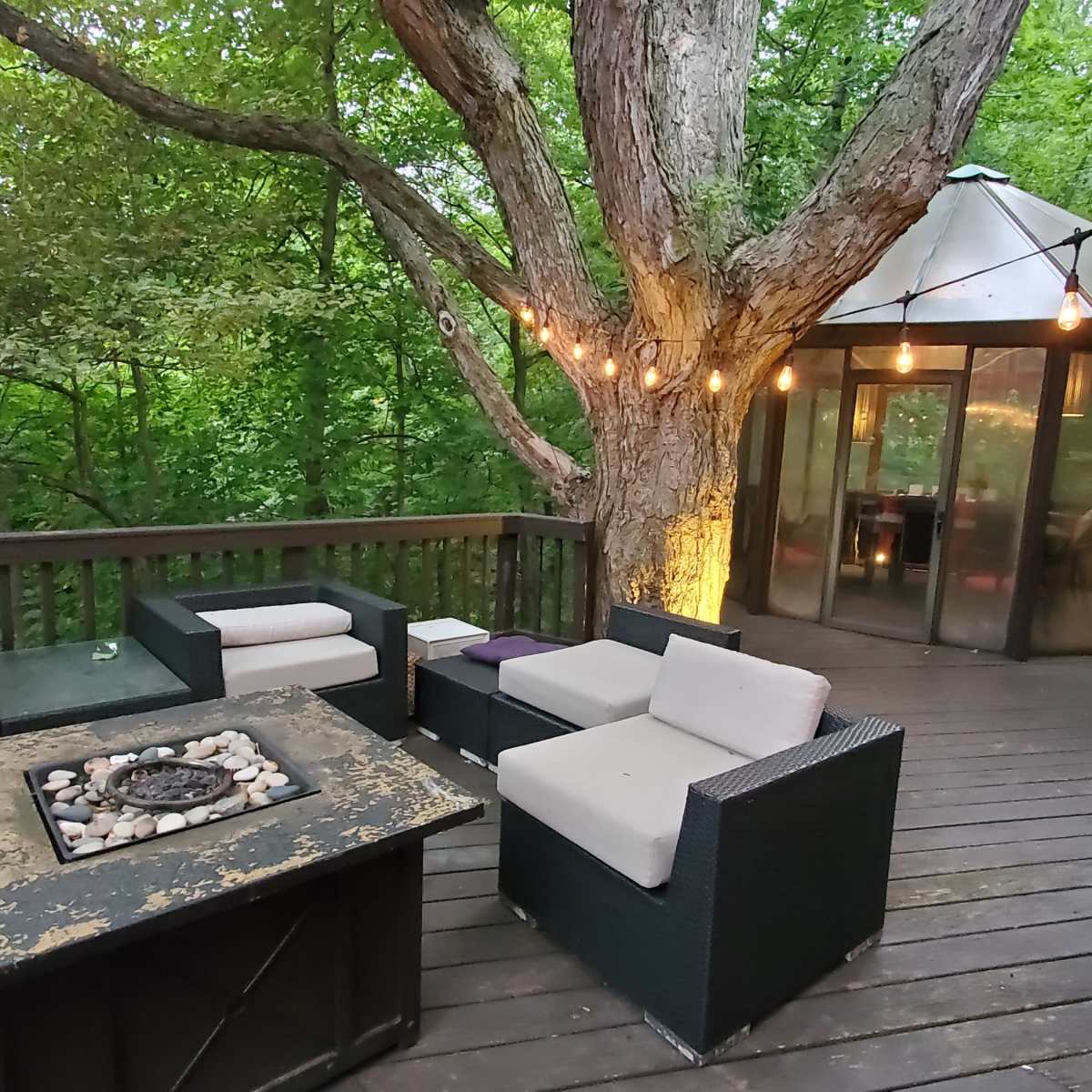 A wooden deck surrounded by trees features modern outdoor furniture and a circular glass-enclosed structure.