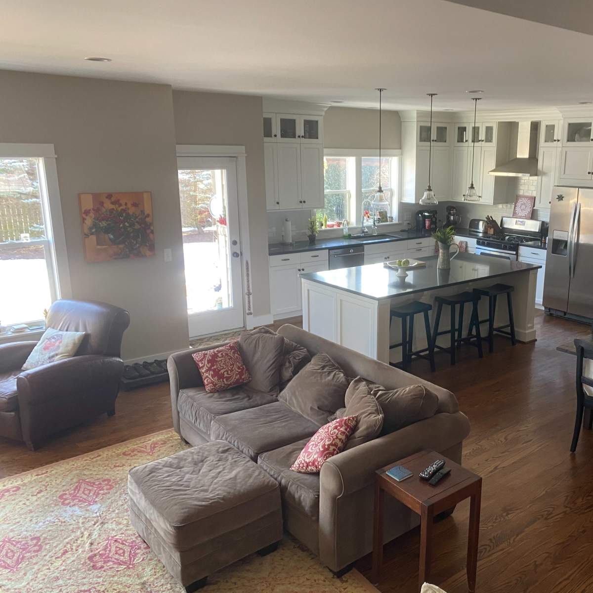 A spacious kitchen and dining area features white cabinetry, wooden flooring, and a mix of seating options, including a sectional sofa and a dining table.