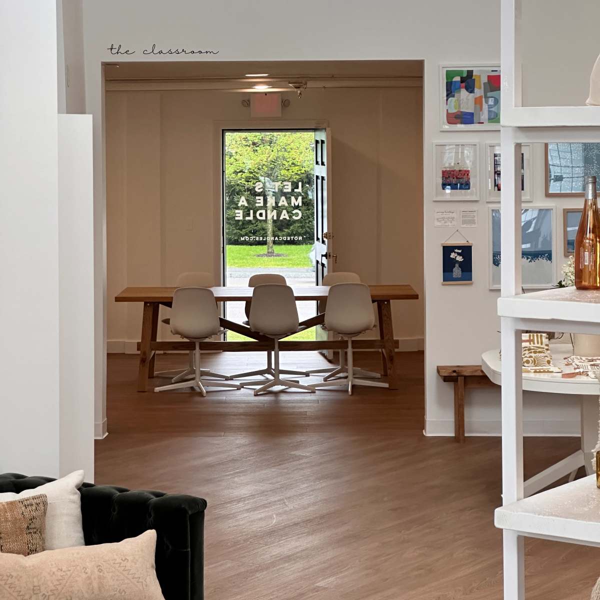 A spacious interior features a large wooden table with three white chairs in a well-lit area, leading to a glass door that opens to the outdoors.