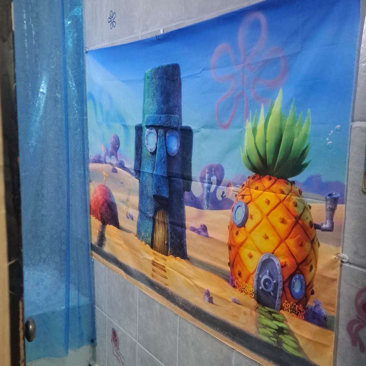 A bathroom with a colorful wall banner depicting SpongeBob SquarePants' pineapple house and Squidward's house.