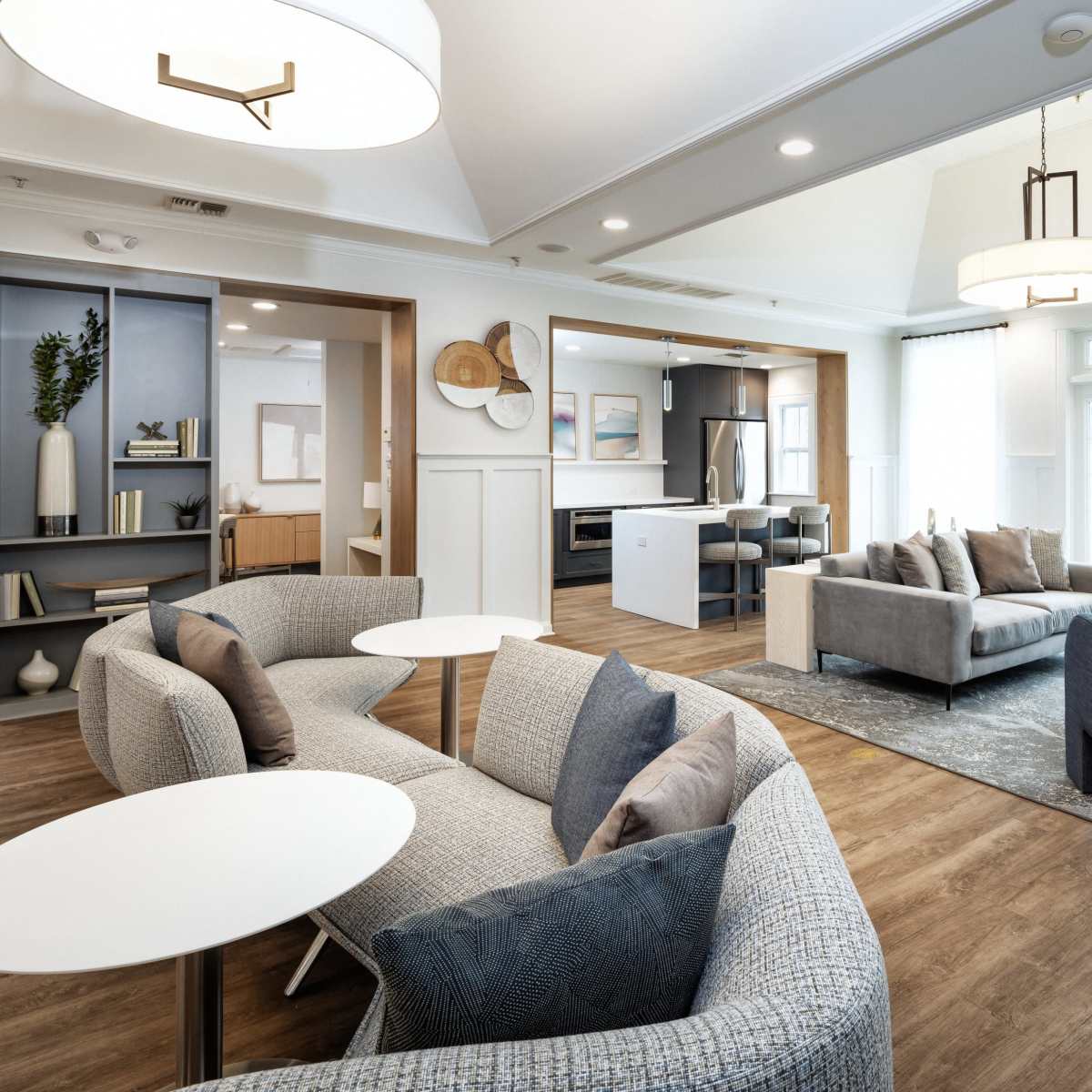 A modern lounge area with several seating arrangements, including curved sofas, armchairs, and small tables, set in a well-lit space with large windows.