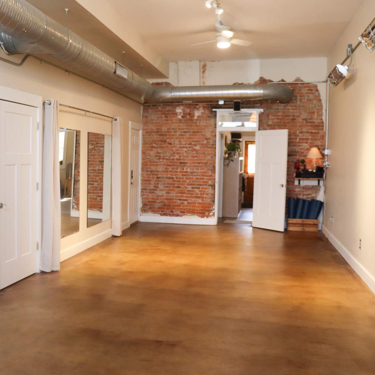 A spacious room with exposed brick walls, large mirrors, and a plant in the corner.