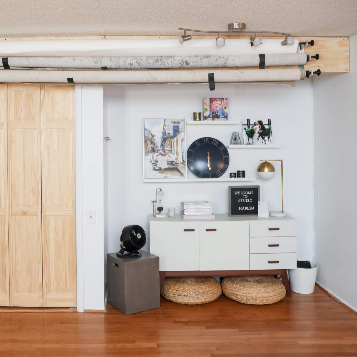 A minimalist room features a wooden closet, a white cabinet with decor, and ceiling-mounted equipment above.