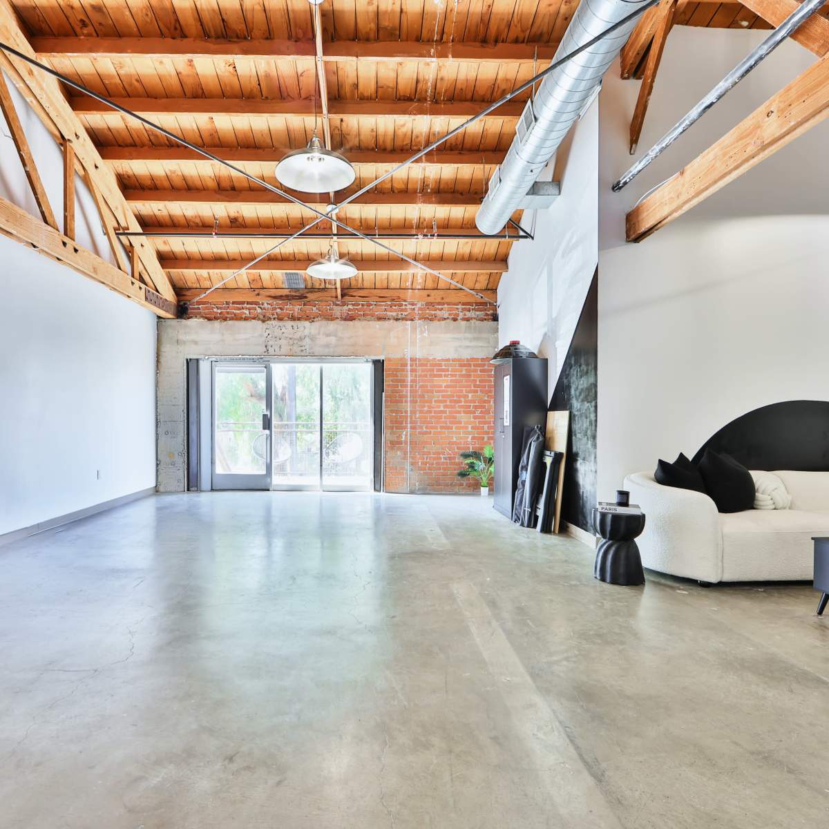 An open interior space with high wooden beams, concrete flooring, and large windows leading to a patio.