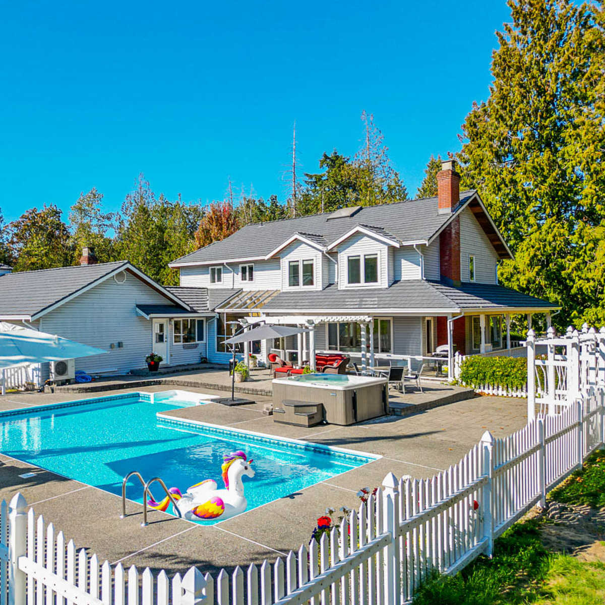 A spacious backyard features a swimming pool with a white fence surrounding a two-story house and landscaped greenery.