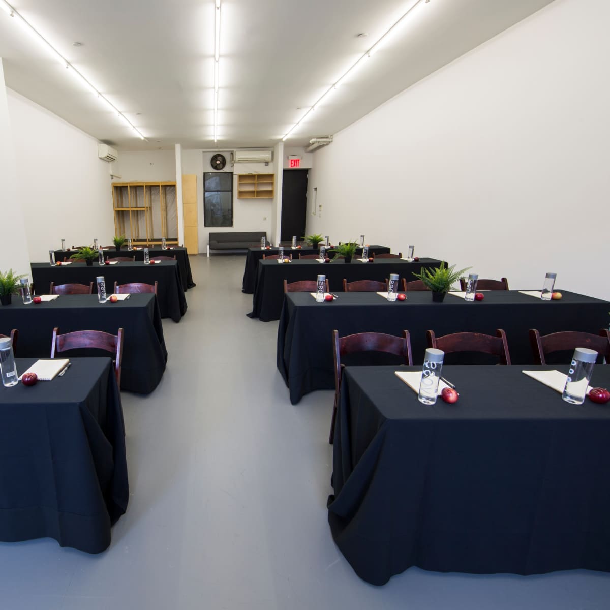 A spacious conference room features multiple tables covered with black linens, each set with water glasses and small plants.