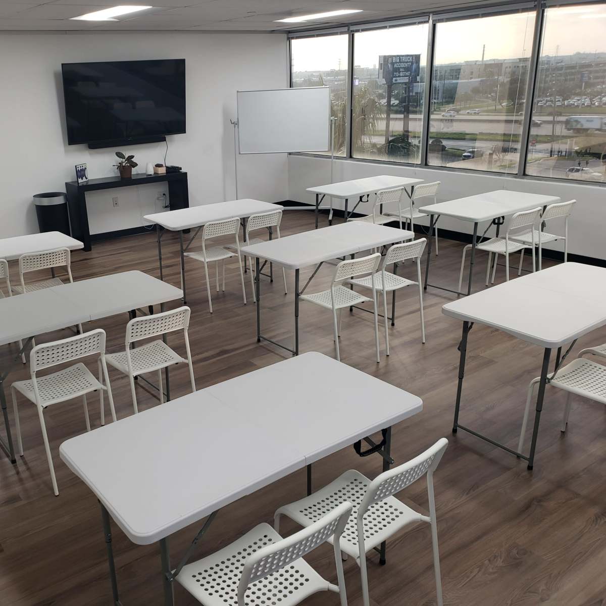 A modern classroom with multiple rows of white tables and chairs arranged in a spacious, well-lit area.