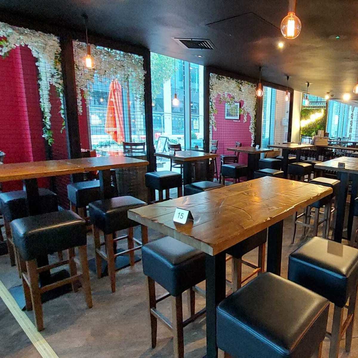 A spacious interior of a restaurant or bar with wooden tables and black leather chairs, illuminated by pendant lights.