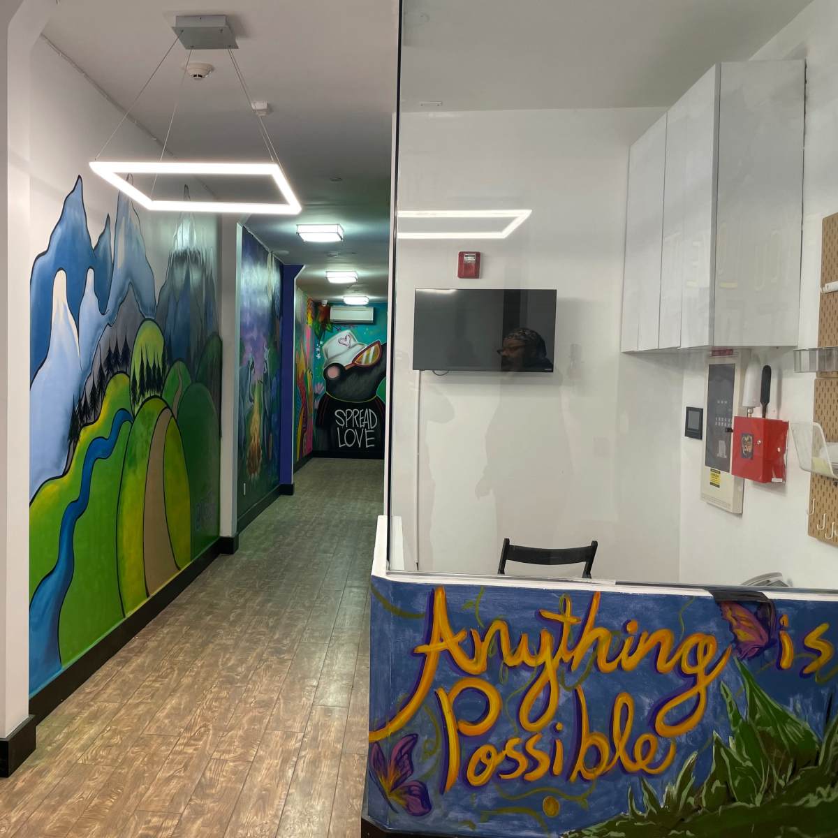 A brightly colored interior hallway with mural art on the walls, leading towards a reception area marked by a welcoming sign.