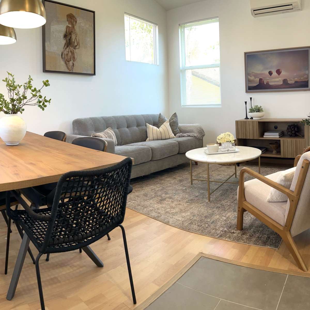 A modern living and dining area featuring a wooden dining table, six black chairs, a gray sofa, a circular coffee table, and decorative artwork on the walls.