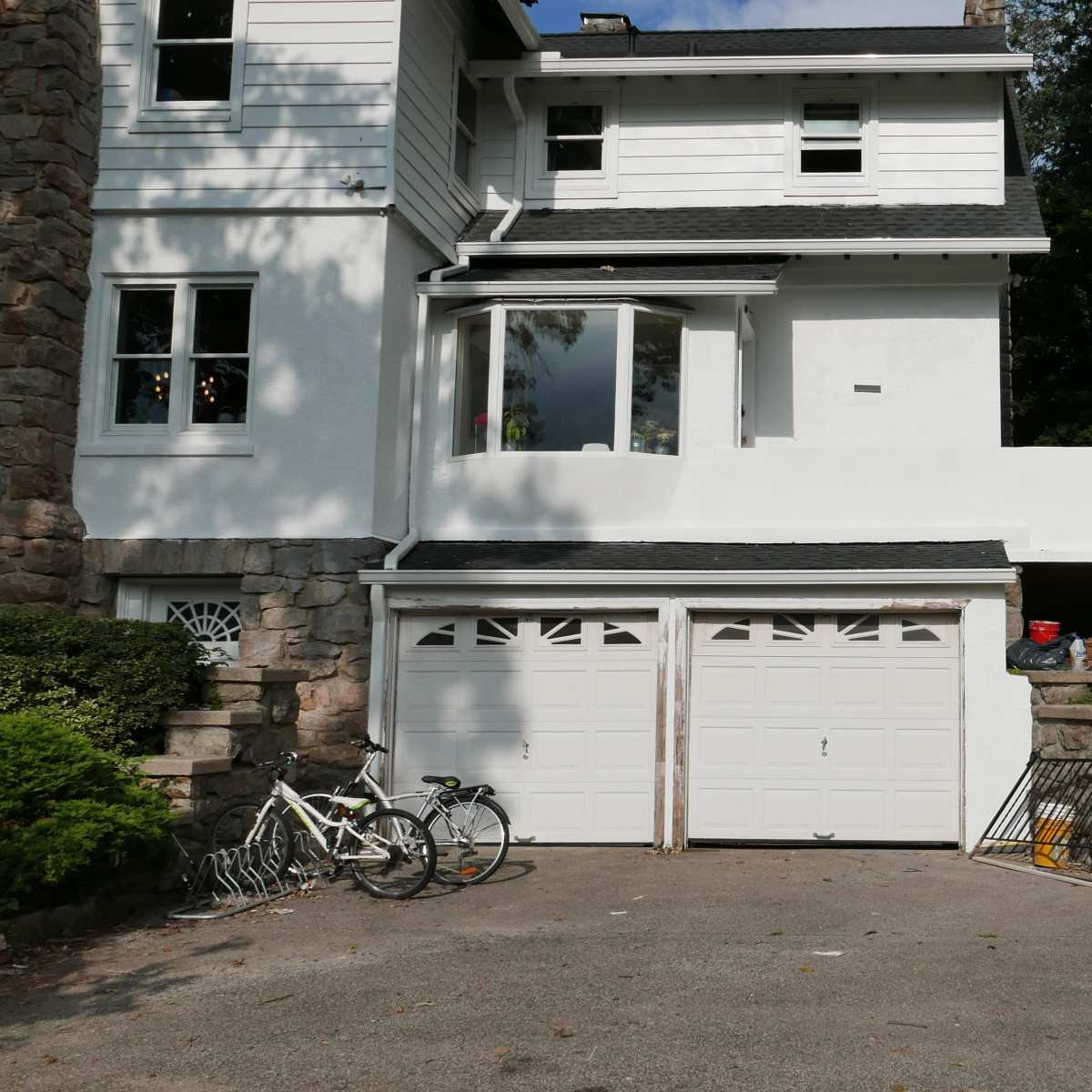A residential building features a two-car garage with bicycles leaning against it, surrounded by a landscaped area and steps leading to the yard.