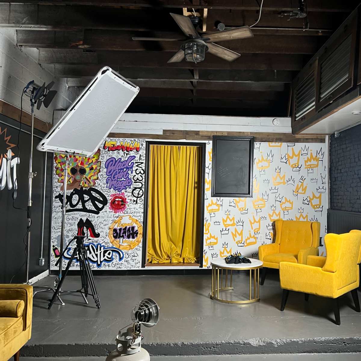 A stylish indoor setting featuring two yellow chairs, a decorative backdrop with graffiti art, and professional lighting equipment.