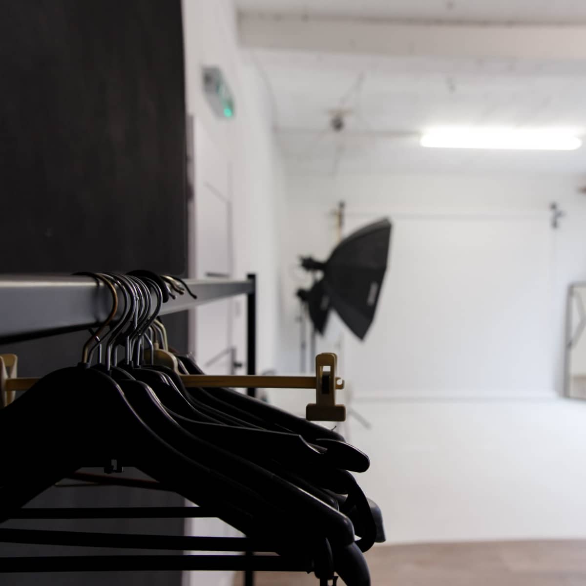 A minimalist photography studio with black clothing hangers in the foreground and lighting equipment positioned in the background.