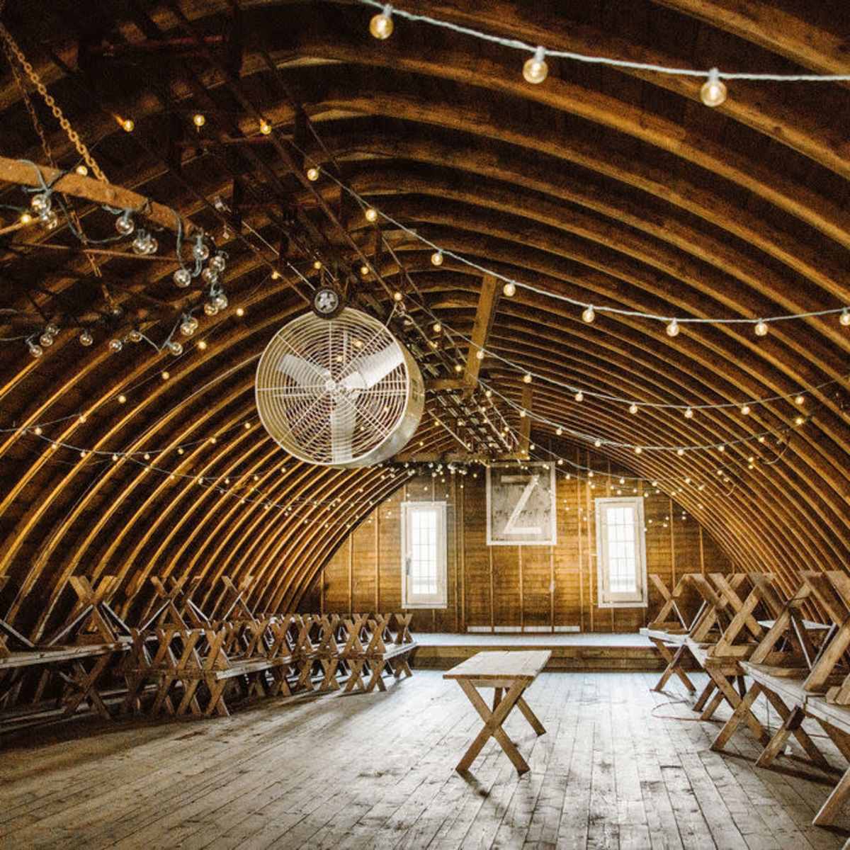 A spacious wooden attic with arched beams, string lights, and folding tables arranged in rows.