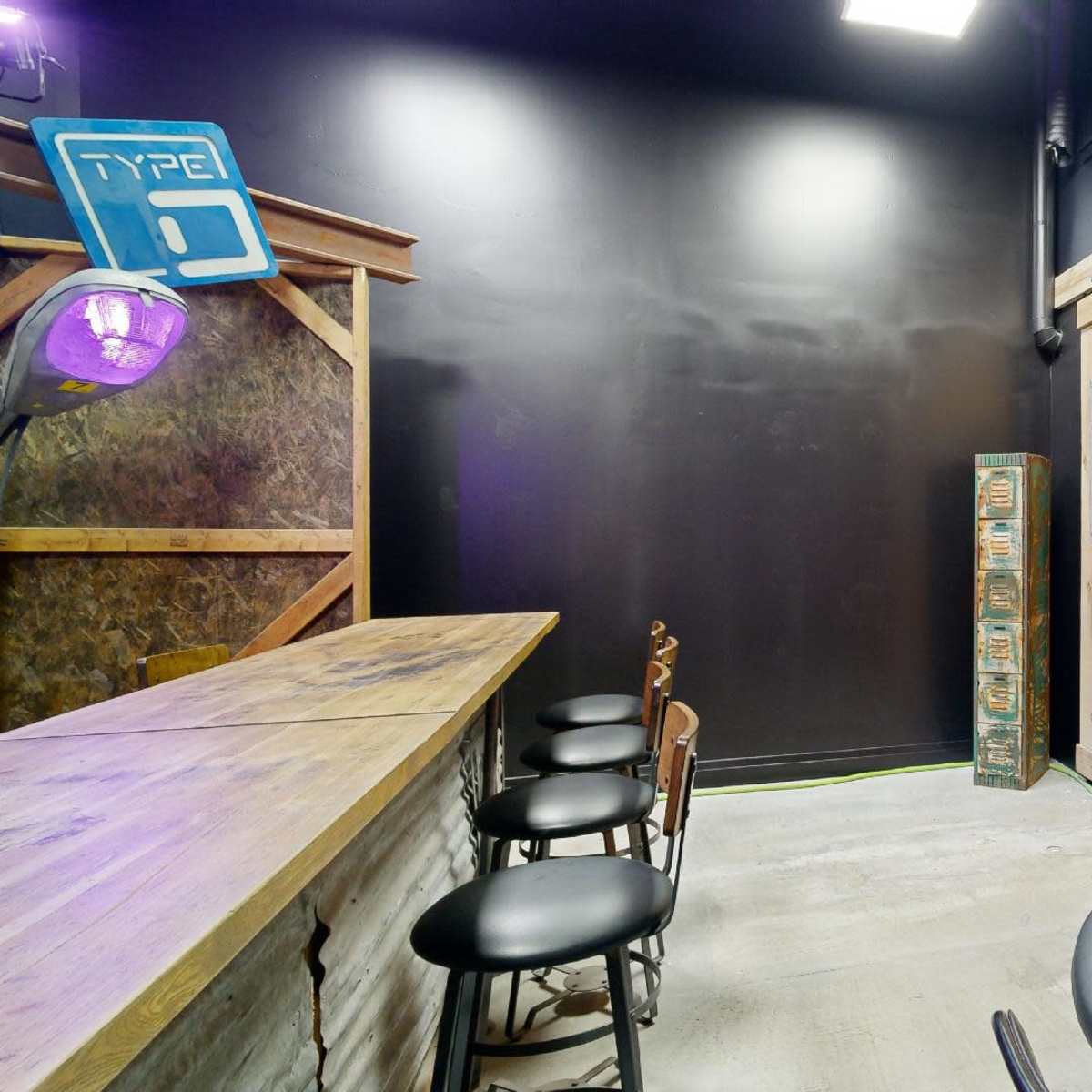 A dimly lit room with a wooden bar, several black stools, and a set of double doors with windows.