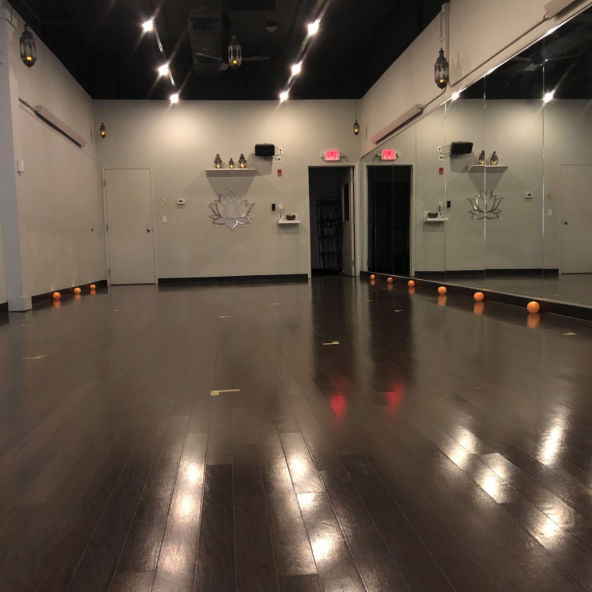 An empty studio with polished wooden floors, mirrors on one wall, and several small orange objects lined up along the floor.
