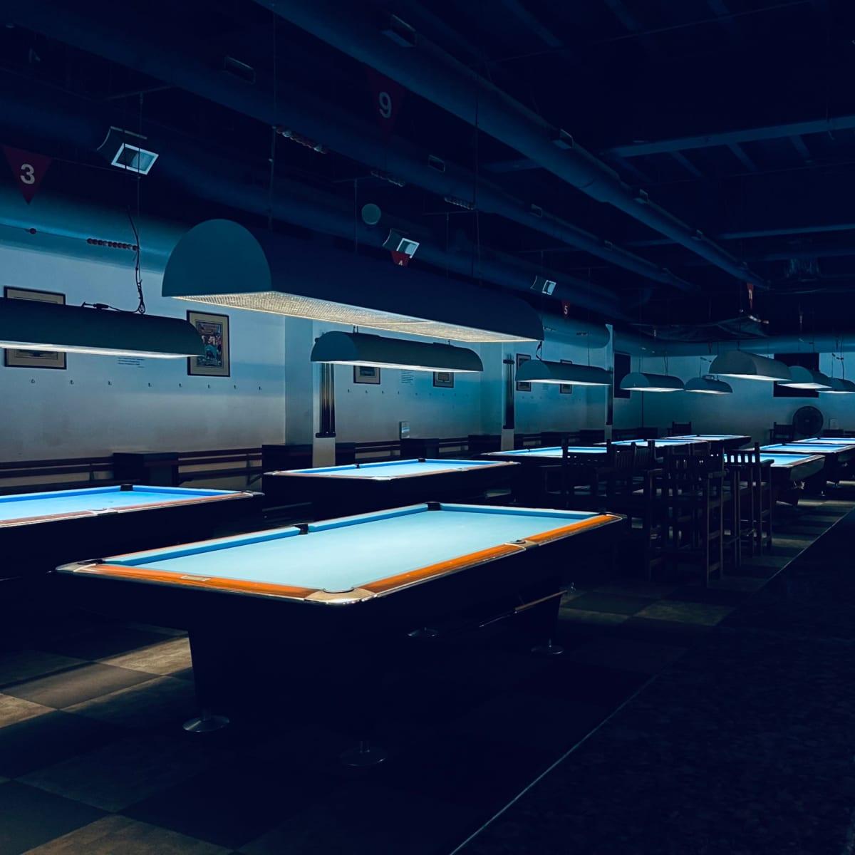An empty billiards hall features several pool tables illuminated by overhead lights.