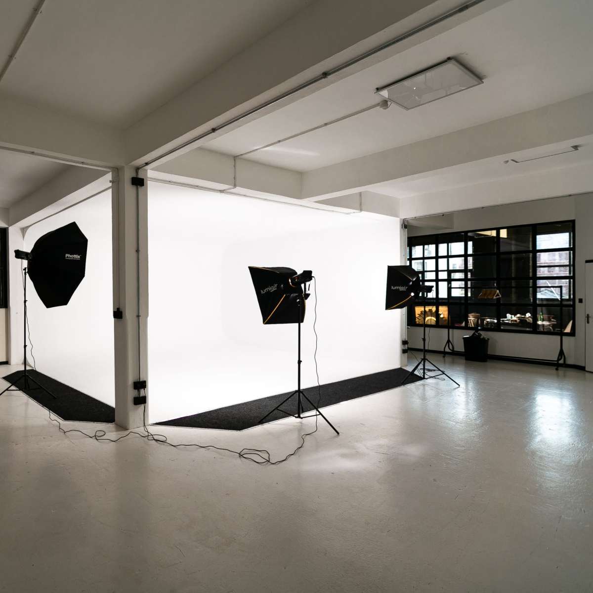 A photography studio features a seamless white backdrop illuminated by several softbox lights and has a minimalist design.