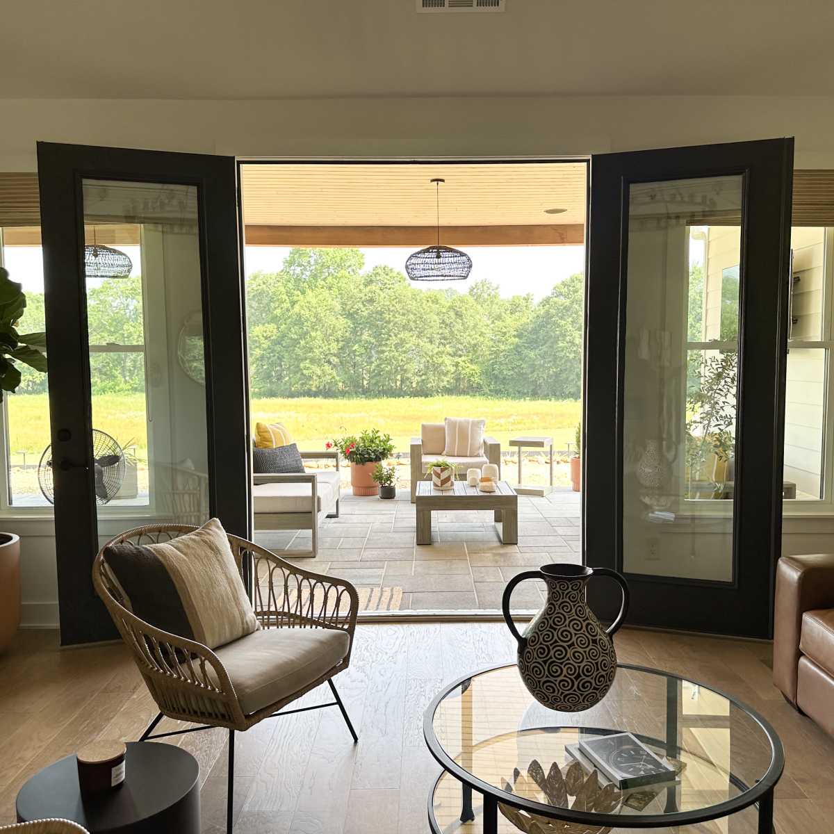 A living room with open double doors leading to a patio area surrounded by greenery.
