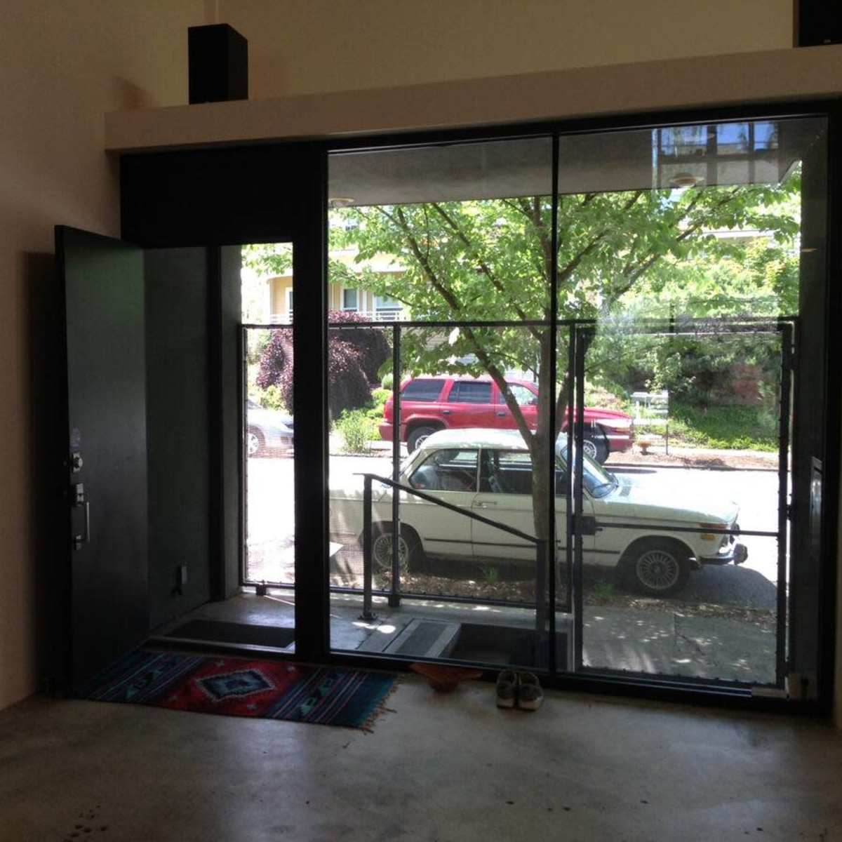 A modern entryway features a large glass door opening to a view of a street lined with trees and a parked car outside.