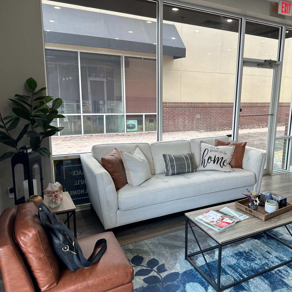 A modern living room with a light-colored sofa, two leather chairs, a coffee table with decorative items, and large windows providing a view outside.