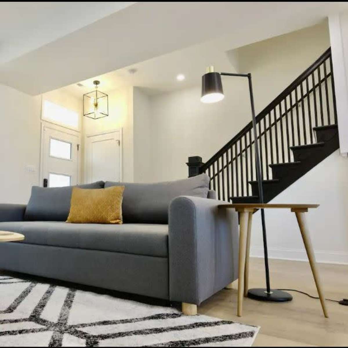 A modern living room with a gray sofa, a round wooden coffee table, a floor lamp, and a staircase in the background.