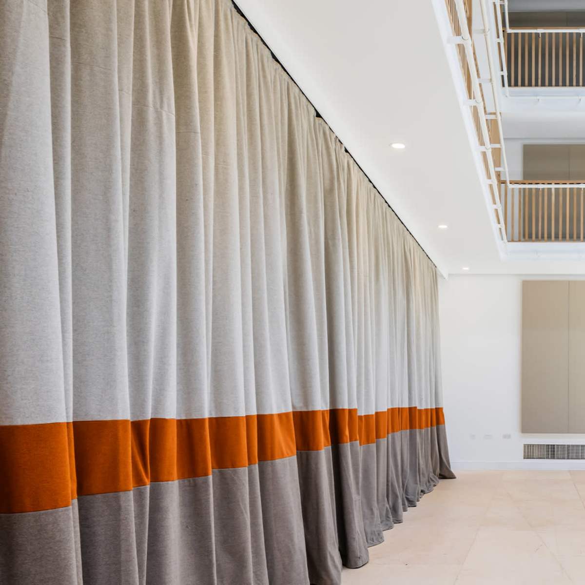 A spacious interior with light-colored walls and a large curtain featuring gray and orange sections, separated by a balcony above.