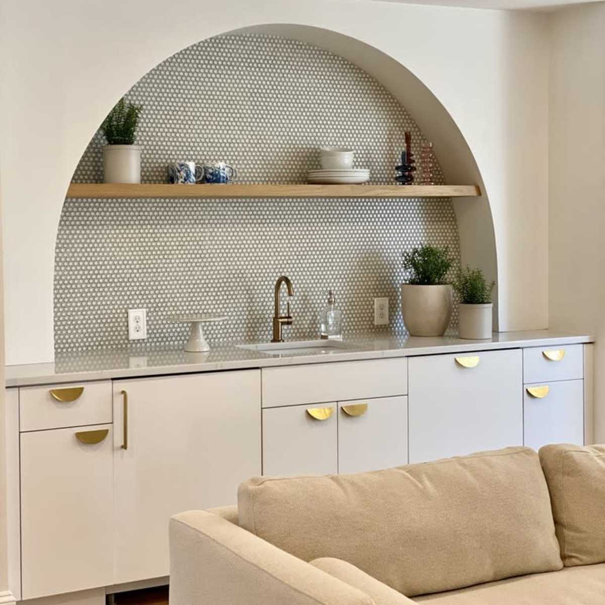 A modern kitchen area with a white cabinet and a patterned tile backsplash featuring an arch shelf displaying decorative items and potted plants.