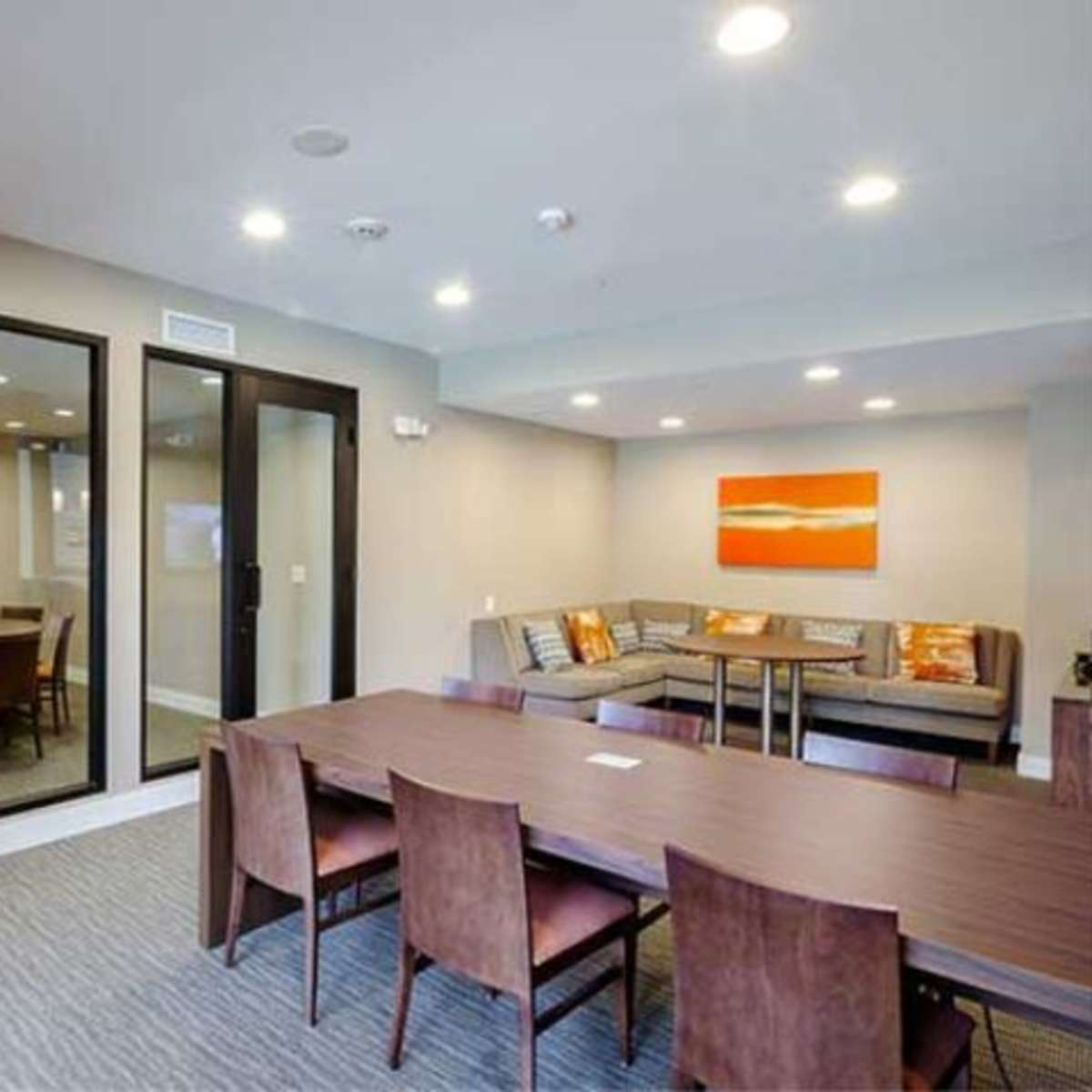 The room features a dining area with a large table surrounded by chairs, a lounge area with a sectional sofa, and a mirror reflecting artwork on the opposite wall.