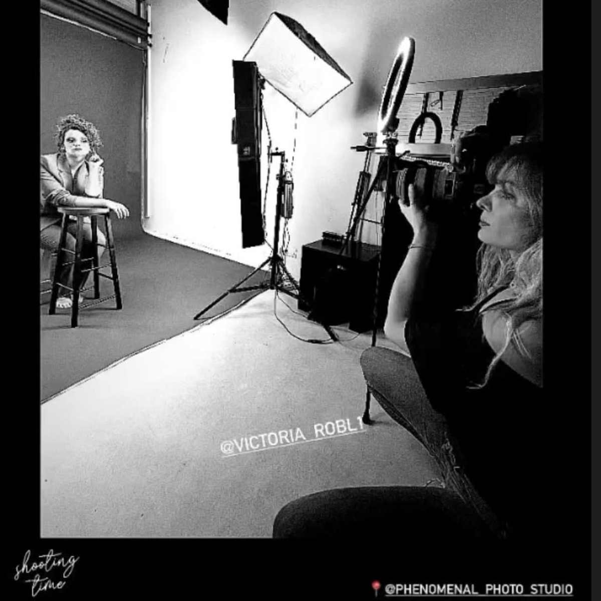 A photographer captures a seated model in a studio, with lighting equipment set up around them.
