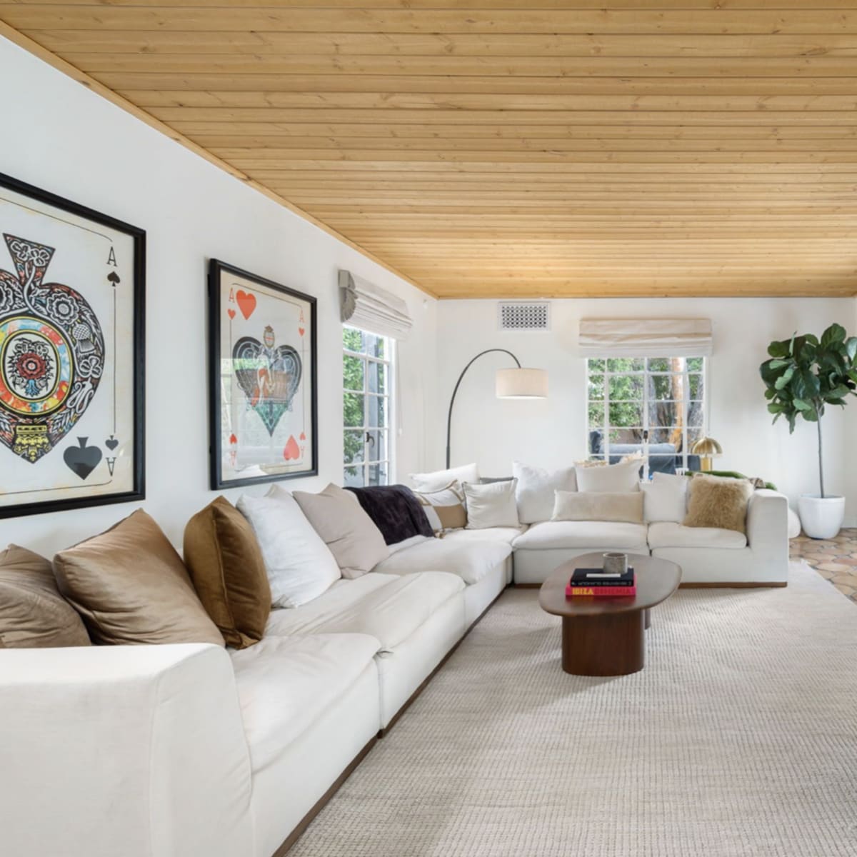 A bright living room features a white sectional sofa, a wooden ceiling, and a cozy fireplace surrounded by decorative art and plants.