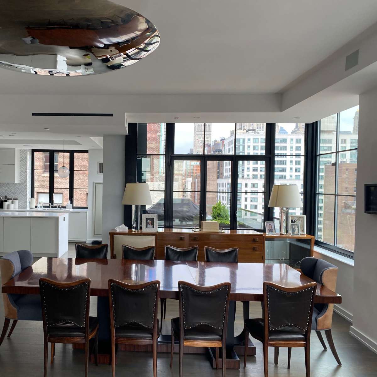 A modern dining area features a large wooden table surrounded by black chairs, with floor-to-ceiling windows offering a city view.