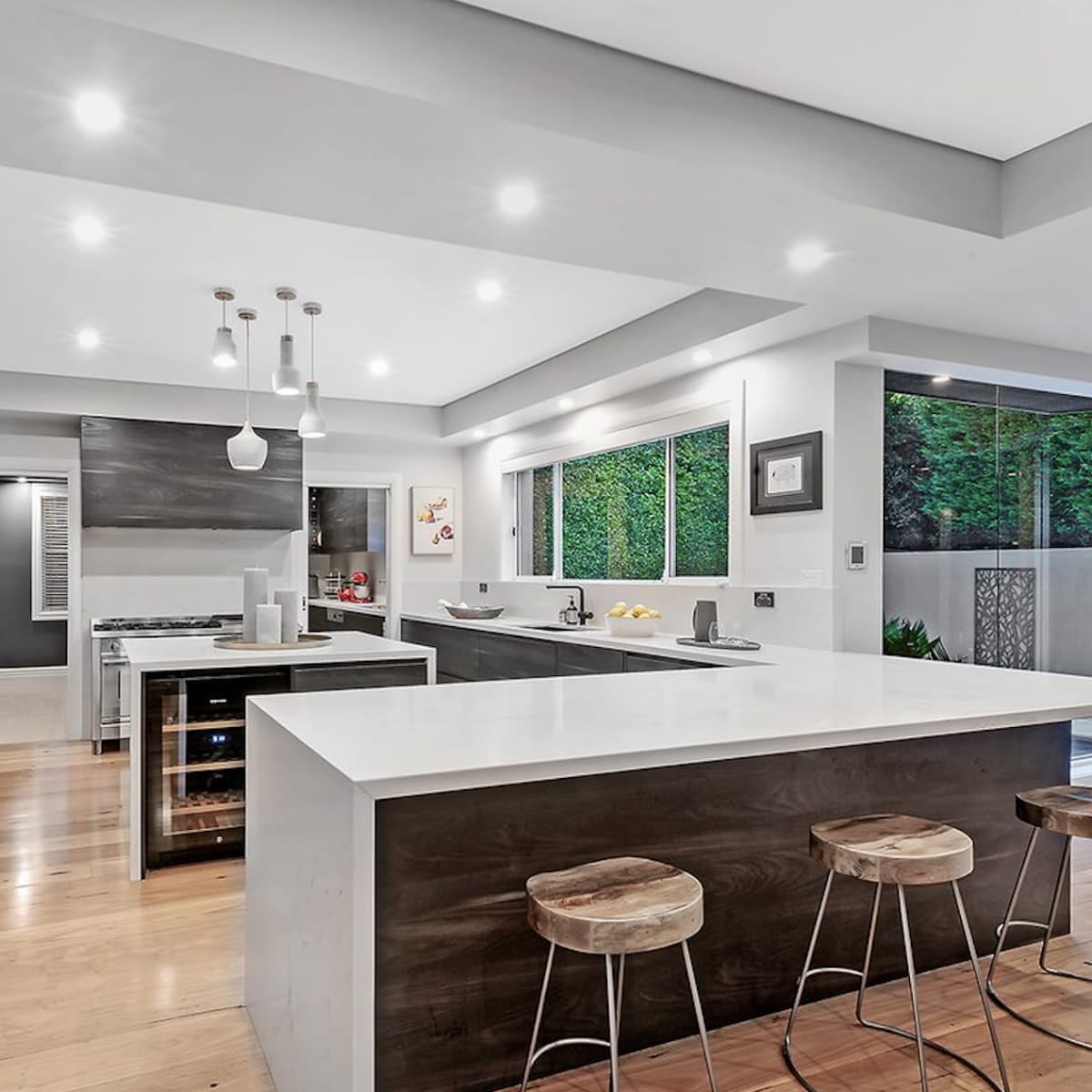 A modern kitchen features sleek cabinetry, a large island with seating, and ample natural light from large windows.