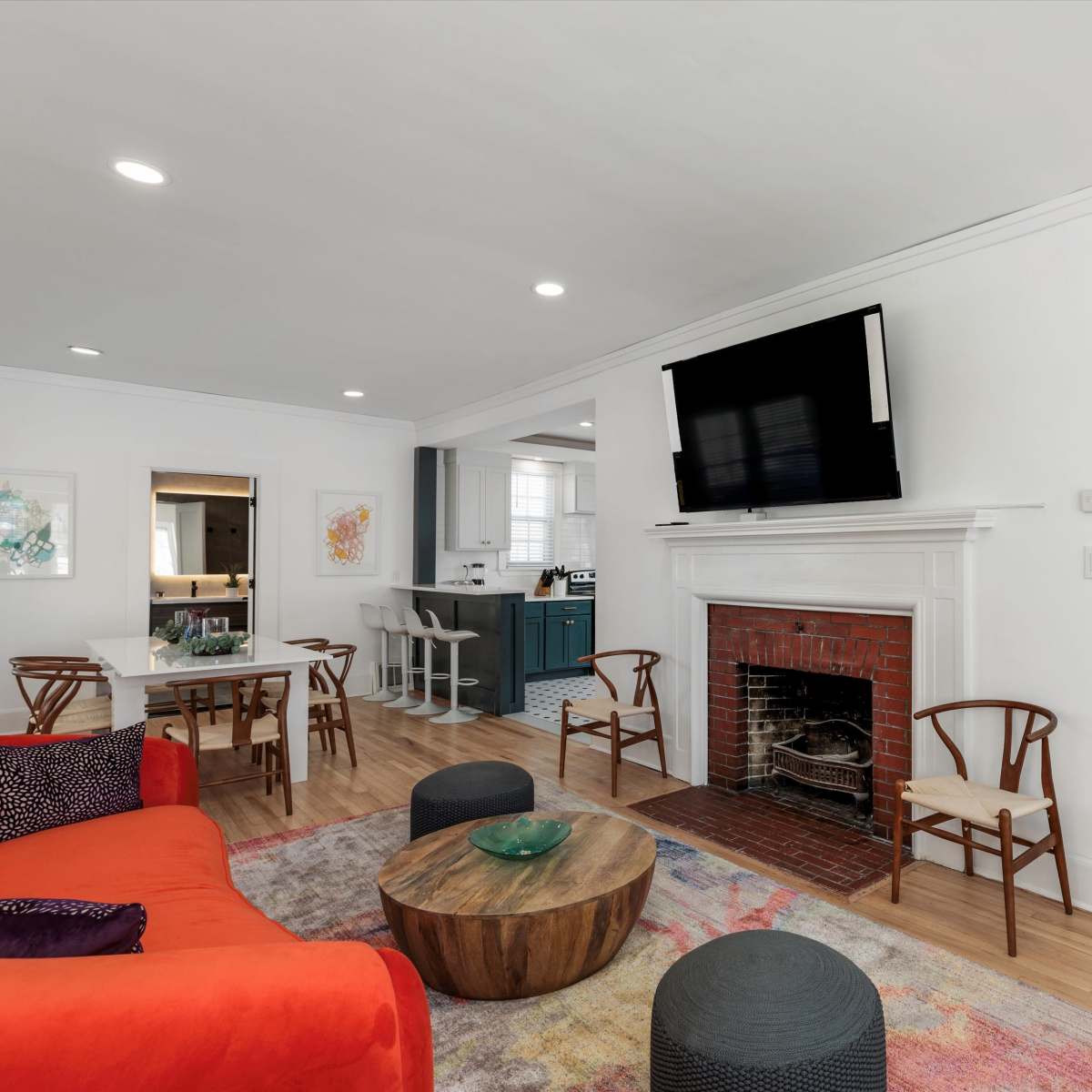 A modern living room with a red sofa, a round wooden coffee table, a brick fireplace, and a flat-screen TV mounted on the wall.