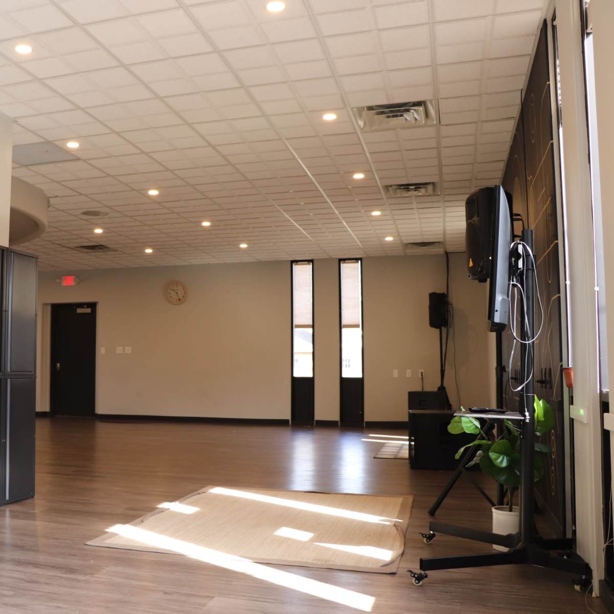 A spacious, well-lit room with wooden flooring, empty lockers on the left, and a television setup on the right.
