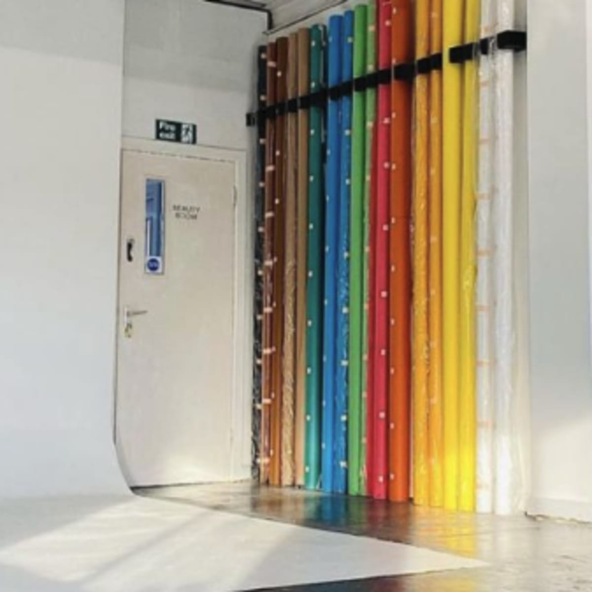 A bright, minimalist interior space featuring a door and a wall adorned with colorful rolled materials.