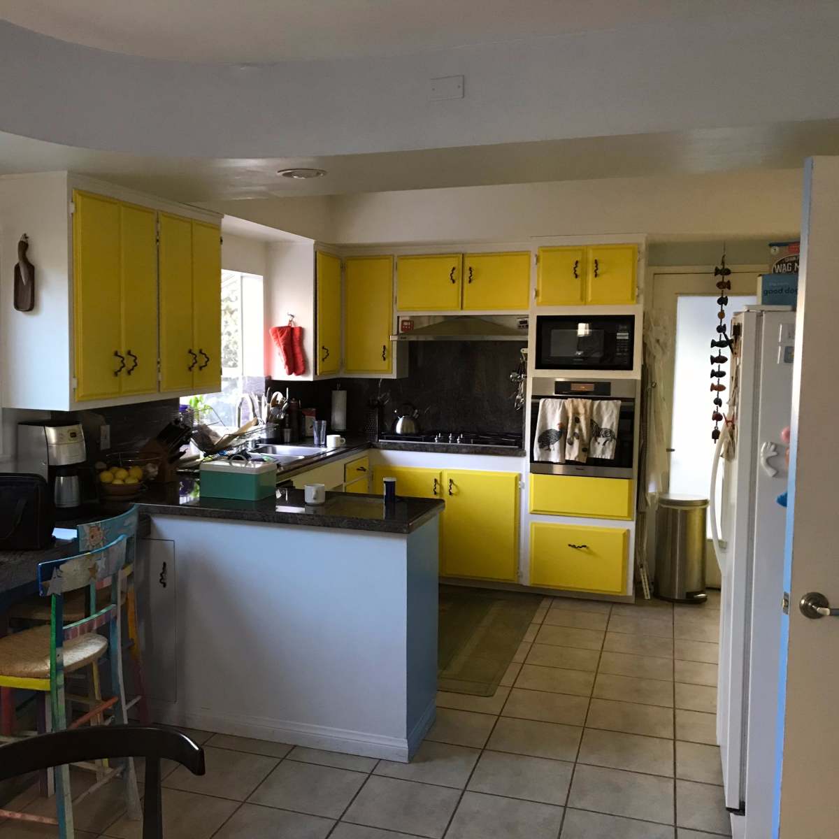 A kitchen with yellow cabinets, a black countertop, and a window overlooking an outdoor space.
