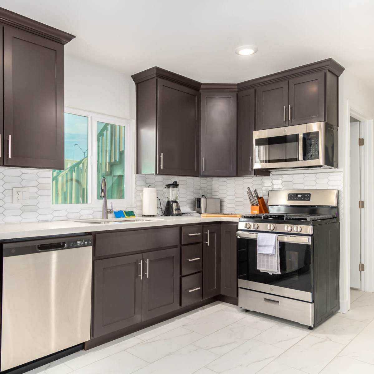 A modern kitchen featuring dark cabinets, stainless steel appliances, and a white tile backsplash.