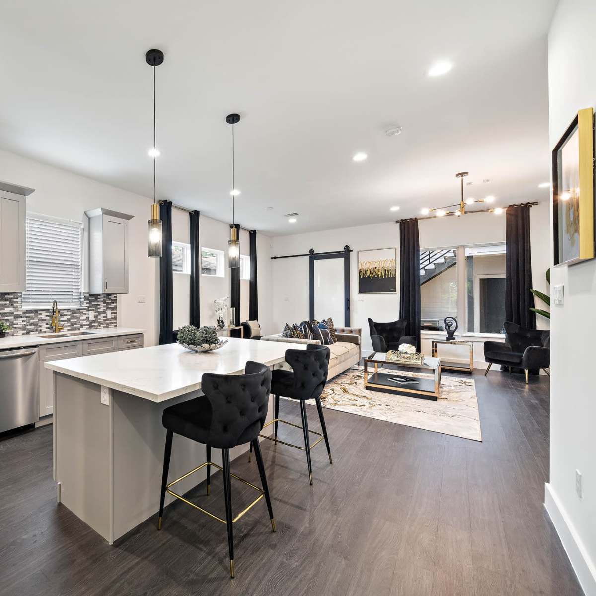 A modern kitchen and living area featuring stainless steel appliances, a stone backsplash, and a central island with bar seating.