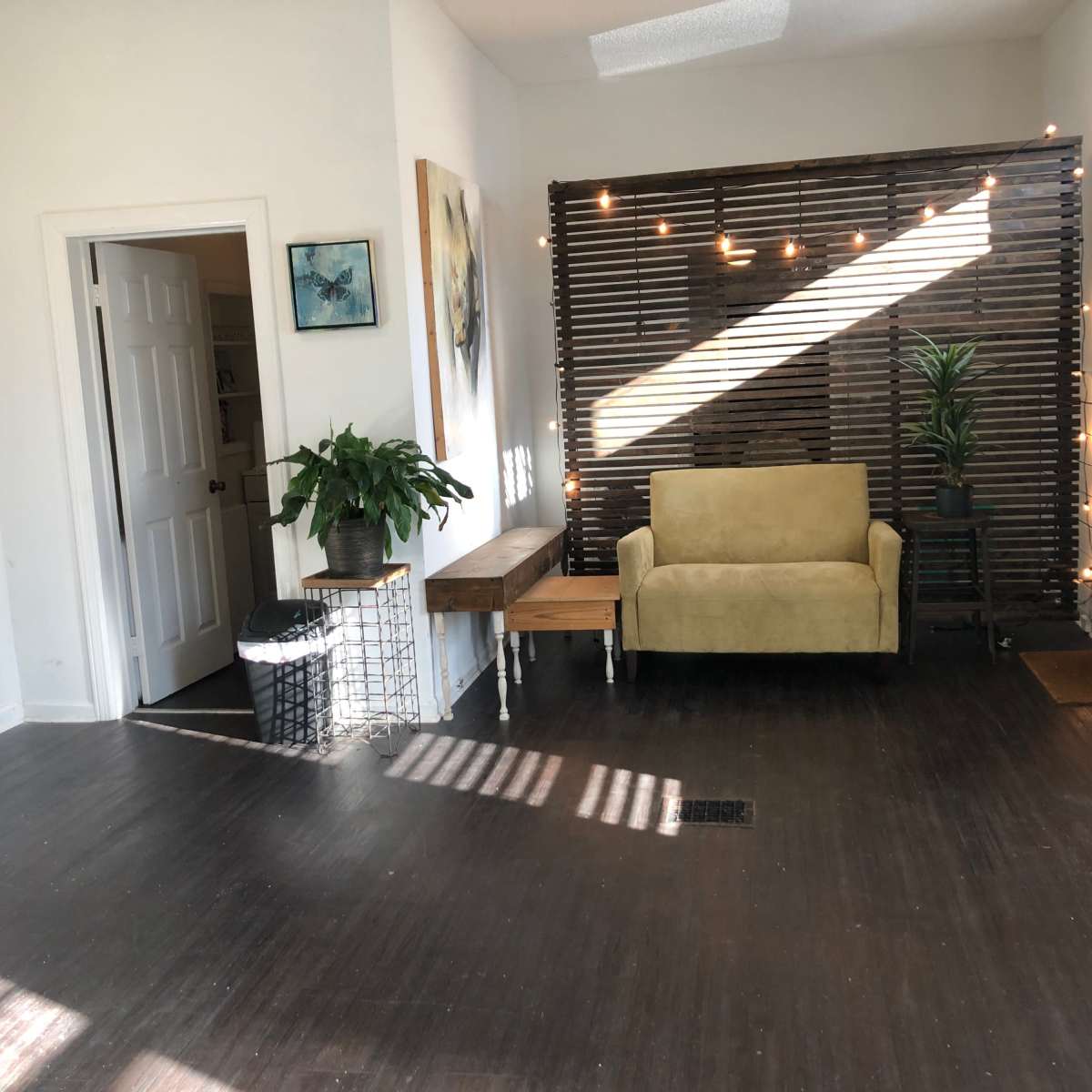 A light-filled room featuring a yellow couch, a wooden table, a potted plant, and a decorative wooden wall with soft lighting.