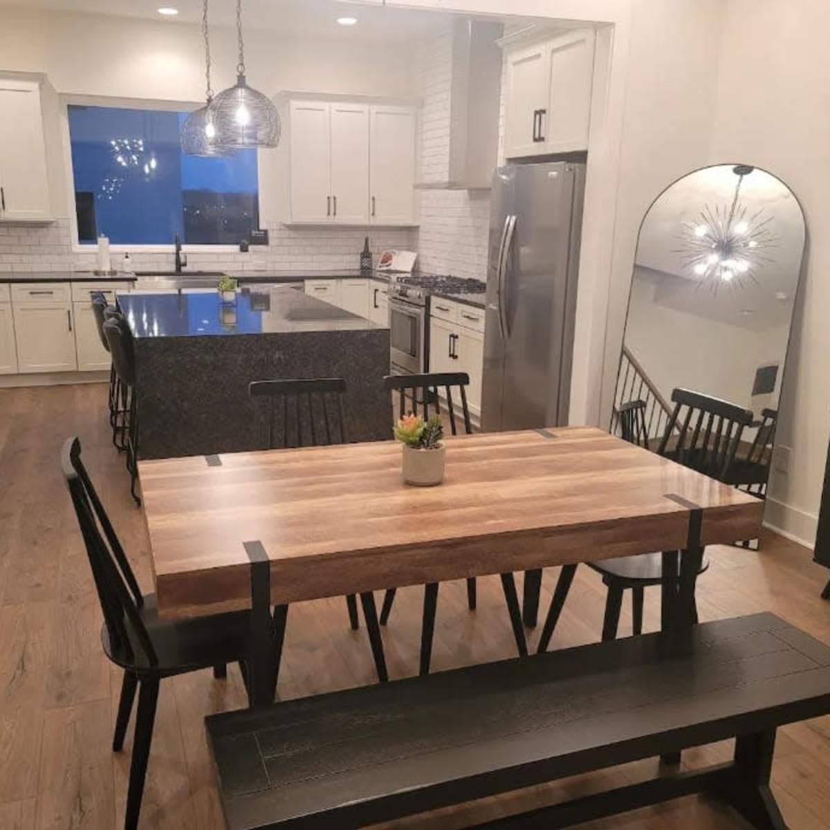 A modern kitchen and dining area with a wooden dining table, black chairs, a large kitchen island, and stainless steel appliances.