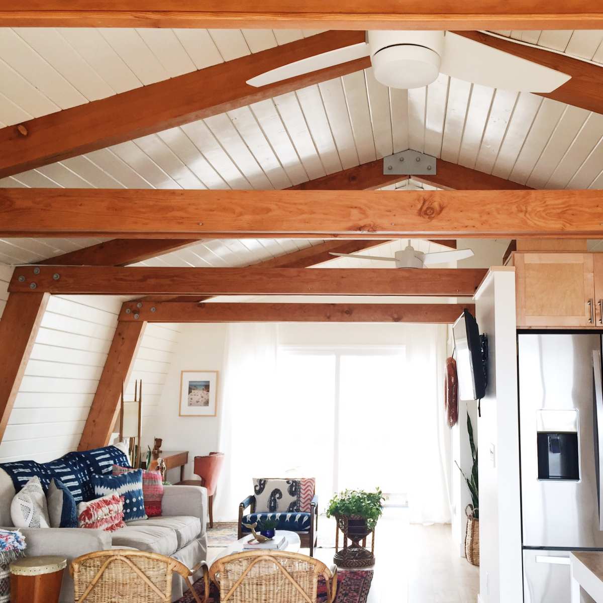 A modern interior of a house featuring exposed wooden beams, a kitchen area with stainless steel appliances, and a cozy living space furnished with a couch and decorative elements.