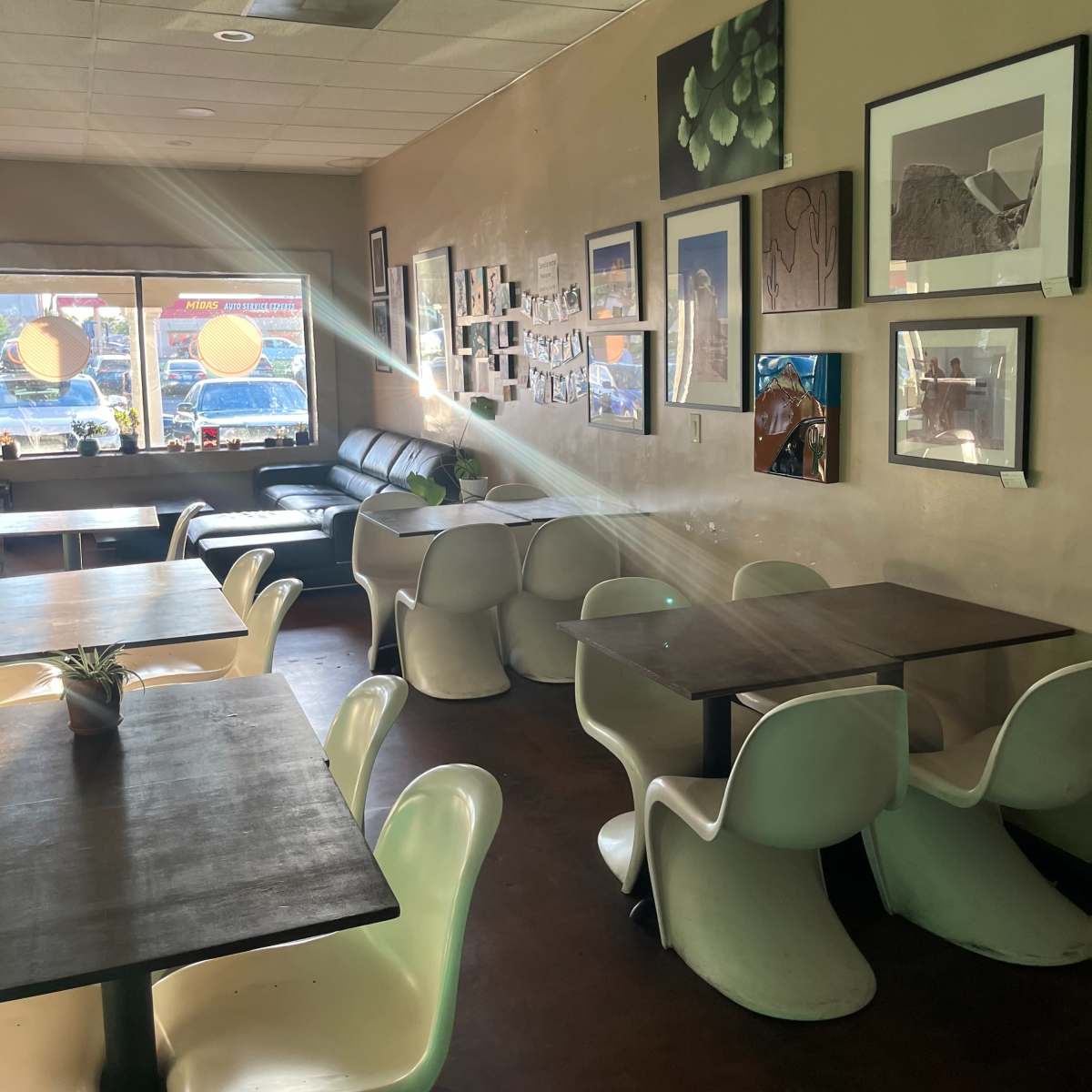 A cozy café interior with wooden tables, white chairs, and walls adorned with various framed artworks.