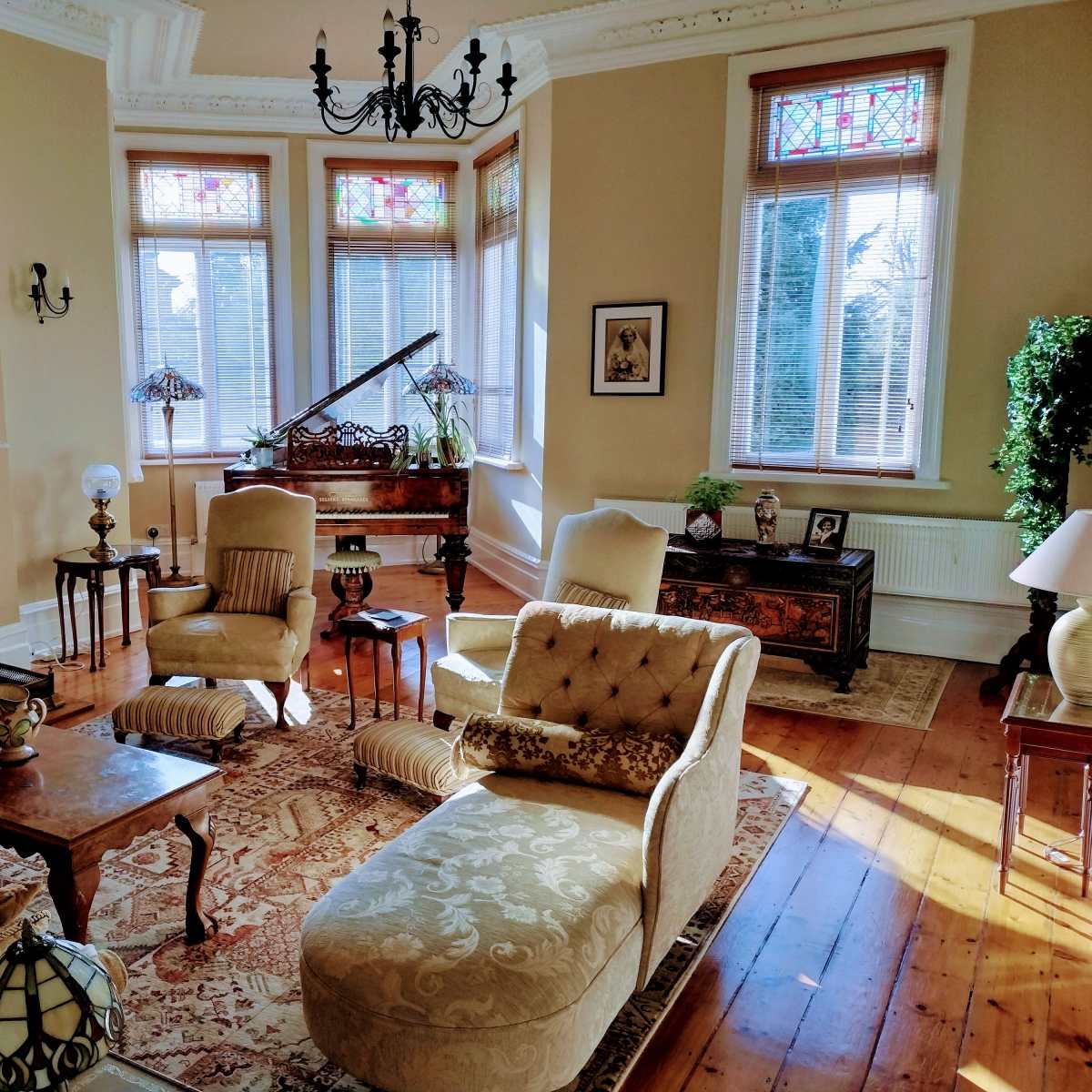 A well-furnished living room with a piano, ornate furniture, a large rug, and decorative stained glass windows.
