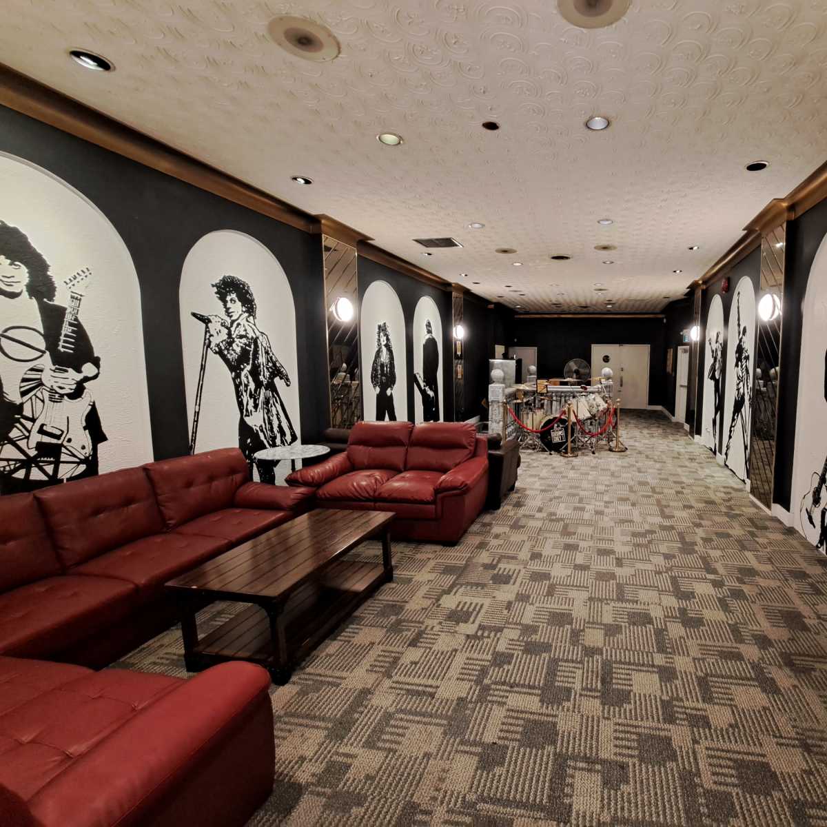 A long room featuring red couches, a coffee table, and large wall murals of musicians on either side.