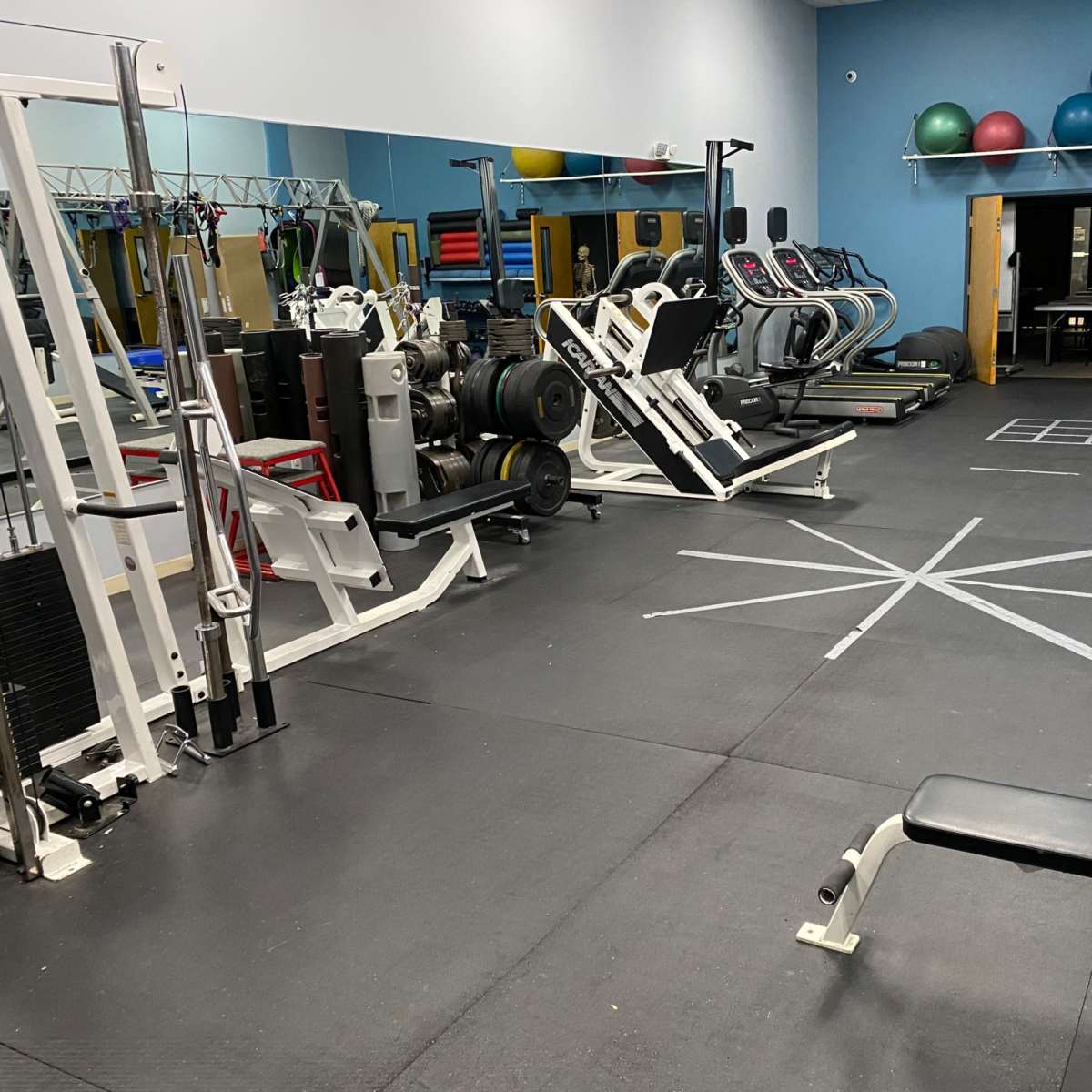 A gym with various exercise equipment, including weight machines, cardio machines, and free weights, arranged in a spacious layout.