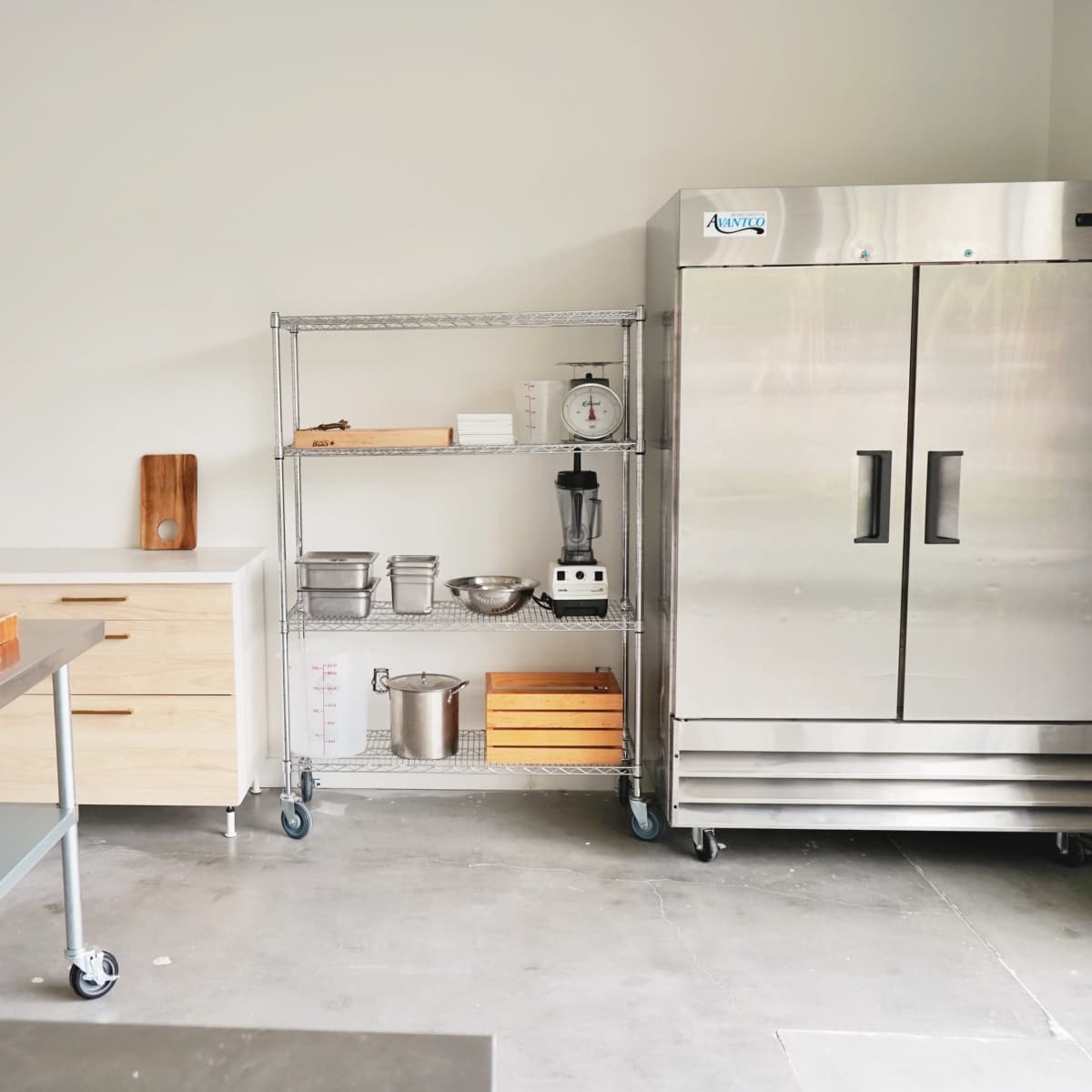 A modern kitchen with a stainless steel refrigerator, a storage cart with kitchen utensils, and a wooden countertop.