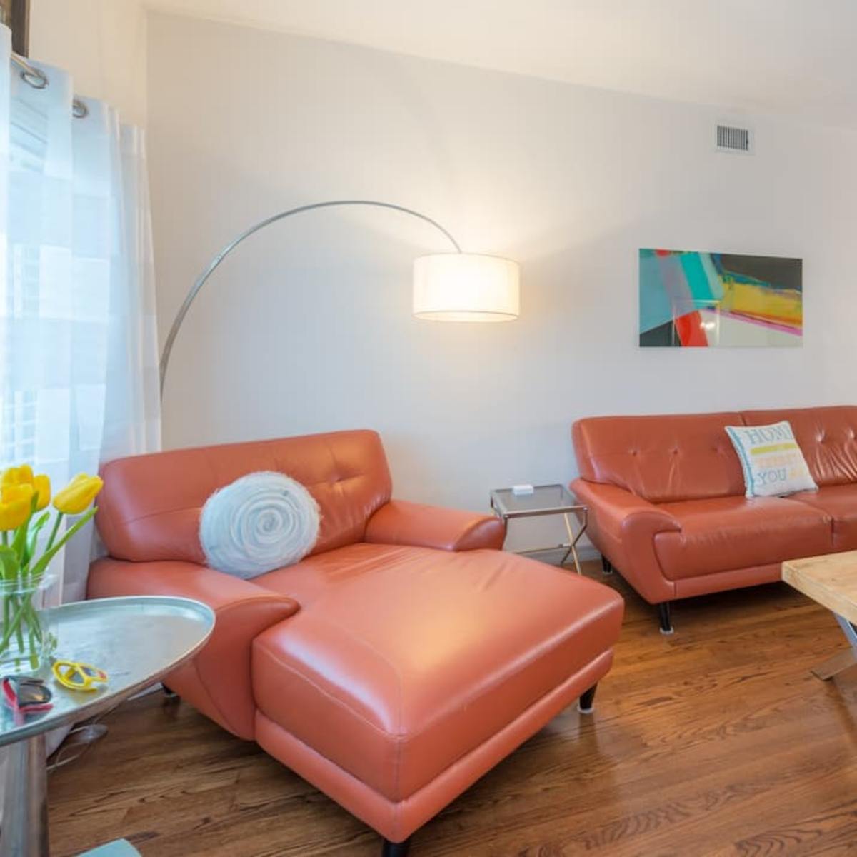 A living room with modern furniture, including two orange couches and a light wooden coffee table, set against a backdrop of white walls and hardwood flooring.