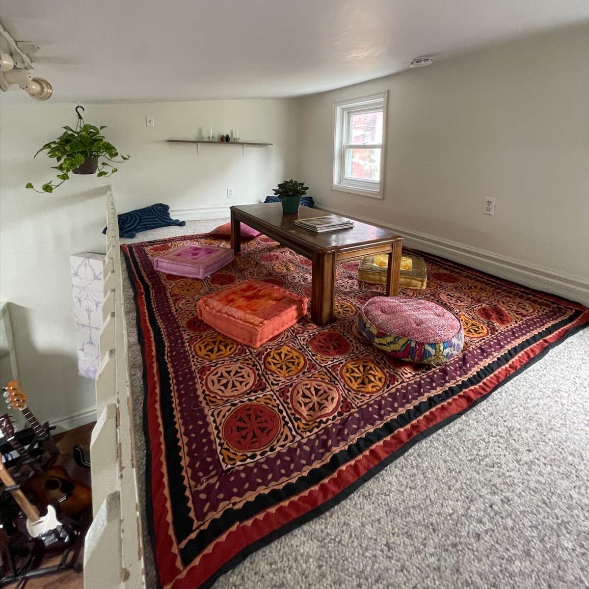 A small, cozy room with a patterned rug, a wooden table, and various cushions arranged for seating.